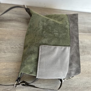 May include: A green, gray, and silver shoulder bag. The bag has a perforated green front, a gray side panel, and a silver pocket. The bag has black straps and silver hardware.
