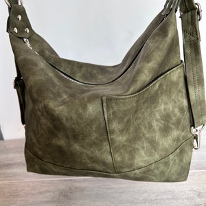 May include: Olive green shoulder bag with a textured finish. The bag features a zippered main compartment, an exterior pocket, and adjustable shoulder strap. Silver-tone hardware accents the bag's design. The bag is made of a durable material.
