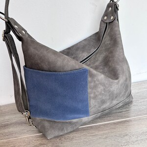 May include: A gray shoulder bag with a blue pocket. The bag has a zipper closure and adjustable straps. The bag is made of a textured material and has silver-colored hardware.