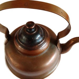 May include: A copper kettle with a black lid and a long handle. The kettle has a traditional design and is perfect for brewing tea or coffee.