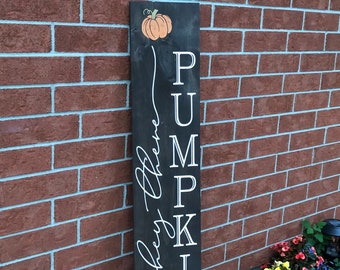 Könnte beinhalten: Ein schwarzes Holzschild mit den Worten "Hey There Pumpkin" in weißer Kursivschrift. Das Wort "Pumpkin" ist vertikal geschrieben, wobei jeder Buchstabe in einem separaten weißen Block steht. Das Schild ist mit zwei orangefarbenen Kürbissen verziert.