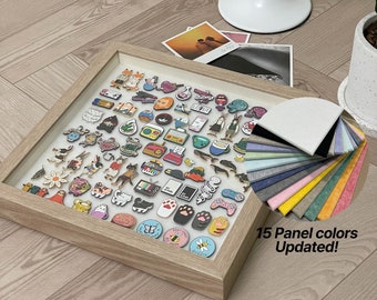 May include: A framed display of colorful enamel pins with various designs, including animals, plants, and abstract shapes. The frame is made of light wood and has a white background. The pins are arranged in a grid pattern. Below the frame is a fan of 15 different colored felt squares, with the text "15 Panel colors Updated!" and a link to the Etsy shop "etsy.com/shop/becosmicstudio".