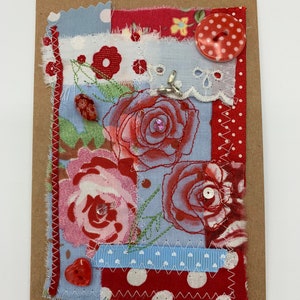 Könnte beinhalten: Handgefertigte Grußkarte mit einer Collage aus Stoffflicken. Das Design zeigt rote Rosen, Tupfen und einen roten herzförmigen Knopf. Die Karte ist mit dekorativen Nähten und einem großen roten Tupfenknopf verziert.