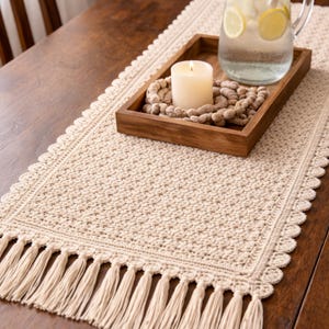 Könnte beinhalten: Beige gehäkelter Tischläufer mit gewelltem Rand und Fransen. Ein Holztablett enthält eine brennende Kerze, dekorative Perlen und eine Glaskaraffe mit Zitronenscheiben. Die Gegenstände befinden sich auf einem dunklen Holztisch.