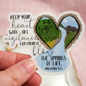May include: White sticker with a heart-shaped design. The heart is divided in half, with a green forest on one side and a blue river flowing through a rocky landscape on the other. The text reads "Keep your heart with all vigilance, for from it flow the springs of life. Proverbs 4:23".