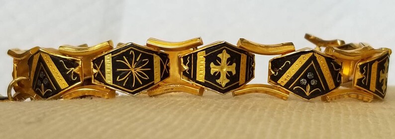 May include: A gold-tone bracelet with black enamel links. Each link features a different geometric design, including a cross, a star, and a diamond shape.