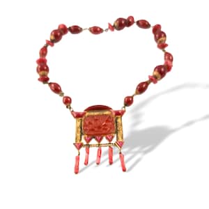May include: A necklace featuring a series of red, oval-shaped beads and a central rectangular pendant. The pendant has a gold-toned frame with a carved red center, accented by small pink triangular details and five dangling red stick-like charms.
