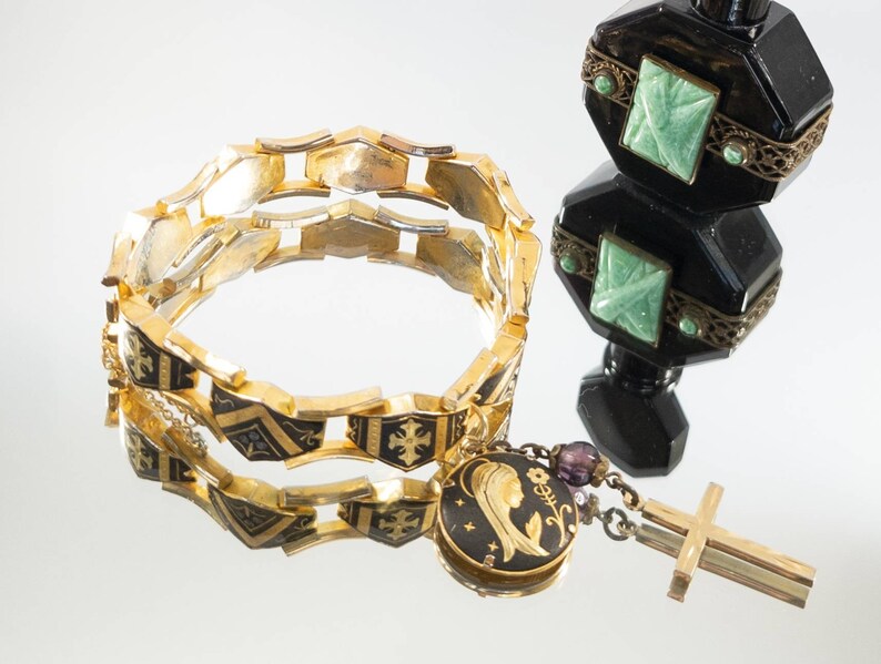 May include: A gold-tone bracelet with black enamel and a pendant featuring a depiction of the Virgin Mary. The pendant is attached to a chain with a small cross charm.
