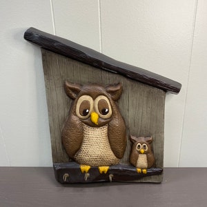 May include: A wooden owl key holder with two owls, one large and one small. The owls are brown and have yellow eyes. The key holder has a brown wooden roof and a brown wooden base.