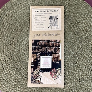 May include: A rectangular tan paper packet labeled ewe & eye & friends, a collection of small counted thread samplers, 5654 So. Prince St. Unit C, Littleton, Co 80120, 303-730-6631, kam slagel & barbara stark. It features the handwritten text June celebration.