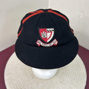 May include: Black wool cap with a red and white embroidered crest. The crest features a castle and the text "NEC SOITE NEC FATIO".