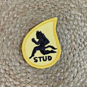 May include: A yellow patch with a black silhouette of a running figure. The word "STUD" is printed in black below the figure. The patch has a teardrop shape with a yellow border.
