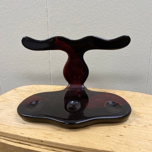 May include: A black and red ceramic stand with three holes for holding razors. The stand has a unique, abstract design.