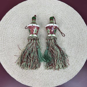 May include: A pair of green and red tassel tiebacks with a star pattern. The tassels are made of a woven fabric and have a ceramic top.