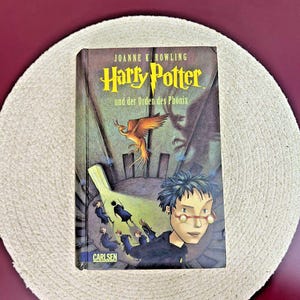 May include: A paperback book cover for "Harry Potter and the Order of the Phoenix" by Joanne K. Rowling. The cover features a dark, shadowy scene with Harry Potter and a phoenix.