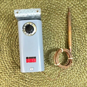 May include: A gray Penn temperature control unit featuring a circular dial with numbers ranging from 50 to 130. The device includes a metal mounting bracket at the top, a red and black label, and a long copper capillary tube coiled with a sensor.
