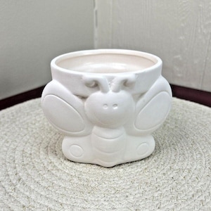 May include: White ceramic planter shaped like a butterfly with a round opening at the top. The planter has a smooth, matte finish.