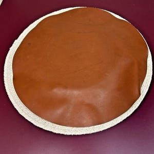 May include: A round brown leather cushion with a white rope border.