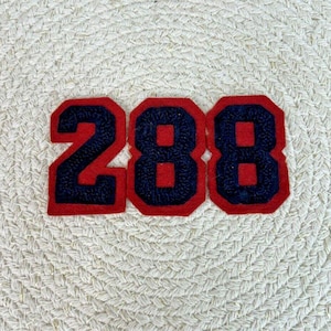 May include: Red felt number patches with a navy blue outline. The numbers are 2, 8, and 8. The patches are on a white woven background.