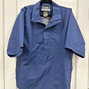 May include: A blue short-sleeved jacket with a collar and a zipper closure. The jacket has the word "ZERO" printed on the collar. The jacket is hanging on a white door.