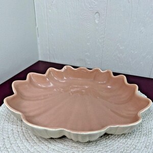 May include: A large, pink ceramic serving dish with a scalloped edge. The dish is shaped like a flower and has a glossy finish.
