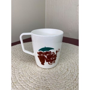 May include: White plastic mug with a brown and green illustration of two bears pushing a cart with an umbrella.