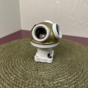 May include: A vintage brass and white multi-bulb light fixture. The fixture has a rounded brass top with three bulb sockets and a white ceramic base. The brass has a slightly aged appearance. The fixture is designed to hold multiple bulbs.