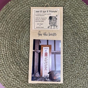 May include: A rectangular craft kit package labeled ewe & eye & friends with a sheep illustration and the text for the birds. It features a photograph of a vertical needlepoint sampler depicting a birdhouse, a blue bird, and floral vines.