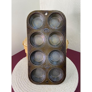 May include: Vintage brown metal muffin tin with six individual cups. The tin has a textured surface and the brand name "EKCO" is embossed on the front.