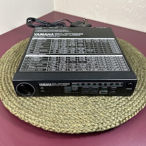 May include: A black Yamaha EMP100 multi-effect processor featuring a top-panel printed effects and parameters list, a front-facing power button, a rotary dial, and a digital display screen with various control buttons and a black power cord.