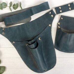 May include: A blue leather tool belt with a large pocket and a smaller pocket on the side. The belt has a metal buckle and is secured with metal rivets.