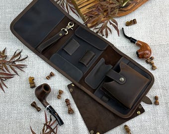 May include: A brown leather pipe case with multiple pockets and a snap closure. The case is open, revealing compartments for pipes and accessories. Two wooden pipes and chess pieces are also visible.