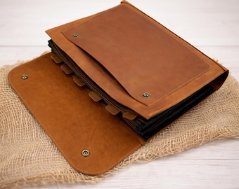 May include: A tan leather document organizer featuring a large flap with a metal snap closure, multiple interior accordion-style dividers, and a rectangular front pocket secured by two metal snaps, showcasing a smooth, matte finish throughout.