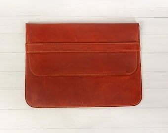 May include: A brown leather laptop sleeve with a flap closure and a stitched design.