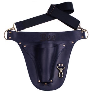 May include: A navy blue leather tool belt with a single pocket and a snap hook. The belt has a black adjustable strap and the word "Bee" is engraved on the front.
