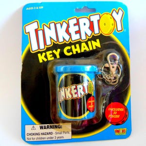 May include: A Tinkertoy key chain in its original blue and black blister pack packaging. The product is a small blue cylindrical container with the Tinkertoy logo, featuring a metal lobster clasp. The packaging includes text stating Ages 3 & Up, Includes 33 Pieces, and a choking hazard warning.