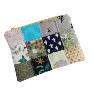 May include: A rectangular zipped pouch constructed from a patchwork of various fabric squares. The patterns include a bee, a hedgehog, cacti, floral motifs, and geometric shapes in colours such as turquoise, navy blue, olive green, and beige.