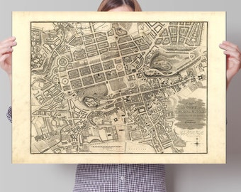 May include: A vintage black and white map of Edinburgh, Scotland, held up by a person. The map, printed on aged paper, details the city's layout with streets, buildings, and landmarks. Text at the bottom reads "Plan of the City of Edinburgh".