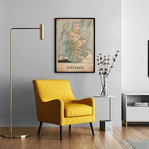 May include: A framed vintage map of Scotland hangs on a gray wall above a yellow armchair. The map features a detailed illustration of the country with various colors and the word "SCOTLAND" at the bottom. A gold floor lamp and a side table with flowers are also in the room.