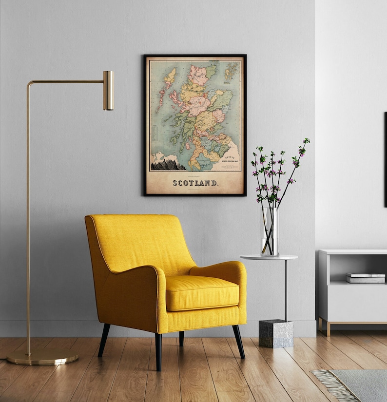 May include: A framed vintage map of Scotland hangs on a gray wall above a yellow armchair. The map features a detailed illustration of the country with various colors and the word "SCOTLAND" at the bottom. A gold floor lamp and a side table with flowers are also in the room.