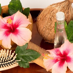 May include: A wooden tray with a coconut, a bottle of clear liquid, two pink hibiscus flowers, a wooden comb, and a wooden hairbrush.