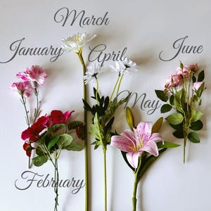 Op de afbeelding: Een verzameling kunstbloemen die maanden vertegenwoordigen, waaronder roze anjers voor januari, rode bloemen voor februari, witte madeliefjes voor maart en april, een roze lelie voor mei en roze rozenknoppen voor juni, met de maandnamen in script.