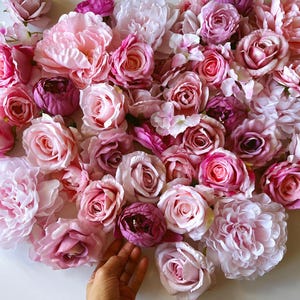 Könnte beinhalten: Eine Anordnung aus künstlichen Blumen in Rosa- und Lilatönen. Rosen und Pfingstrosen sind am prominentesten, mit Farben von Hellrosa bis Dunkellila. Die Blumen befinden sich auf einer weißen Oberfläche.