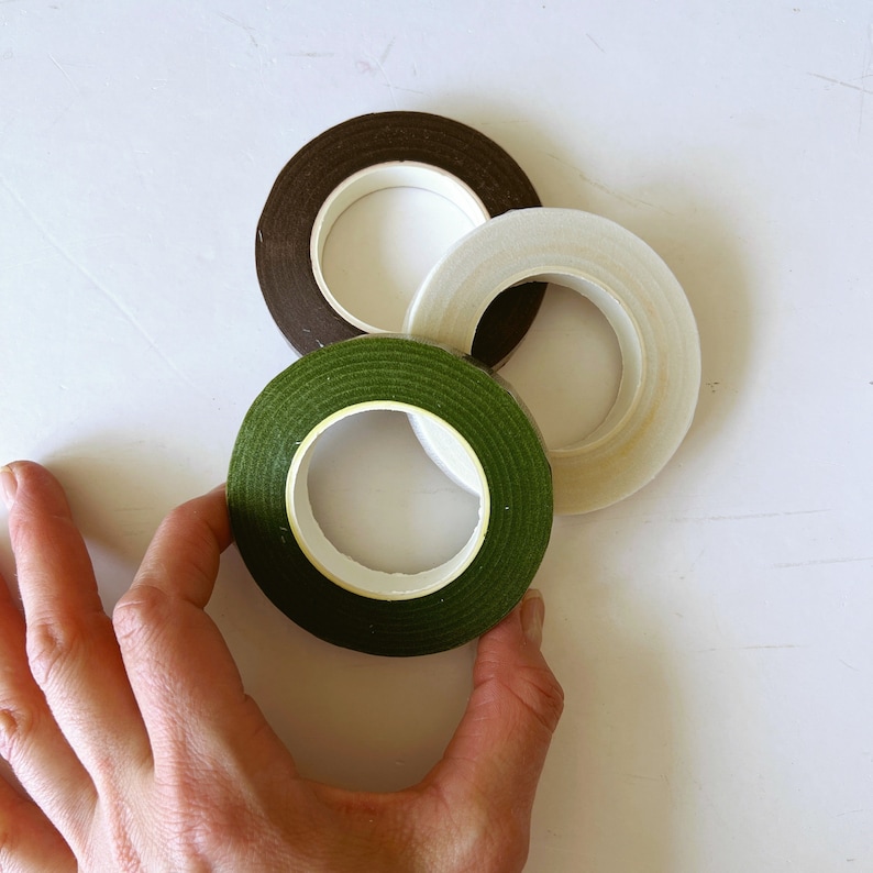 May include: Three rolls of floral tape in dark brown, light green, and white. Each roll features a circular center and a textured surface, arranged in a cluster to display the distinct color variations of the adhesive tape rolls.