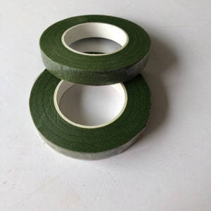 May include: Two rolls of dark green floral tape stacked vertically. Each roll features a matte, textured surface with a white inner core, designed for wrapping stems and creating floral arrangements with a consistent, non-reflective finish.