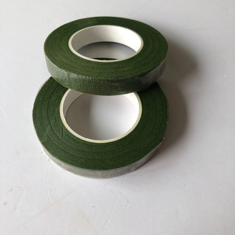 May include: Two rolls of dark green floral tape stacked vertically. Each roll features a matte, textured surface with a white inner core, designed for wrapping stems and creating floral arrangements with a consistent, non-reflective finish.