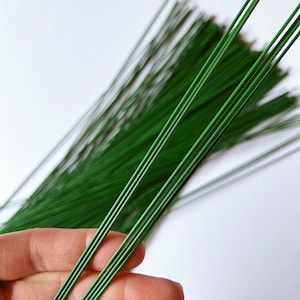 Może przedstawiać: Zbliżenie na wiązkę zielonego drutu florystycznego, trzymaną w dłoni, na białym tle. Drut ma żywy, jednolity zielony kolor. Obraz podkreśla fakturę i kolor drutu, odpowiedni do rękodzieła i kompozycji kwiatowych.