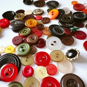 Puede incluir: Una colección de botones variados en diferentes tamaños, formas y colores. Los botones incluyen rojo, negro, marrón, amarillo, verde y blanco. Algunos botones tienen dos agujeros, otros cuatro. Los botones son de plástico y otros materiales.