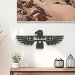 May include: Black metal wall art featuring a stylised eagle with outstretched wings. The eagle is a popular symbol of freedom and strength. The art is mounted on a white wall above a wooden shelf with books, a plant, and other decorative items.