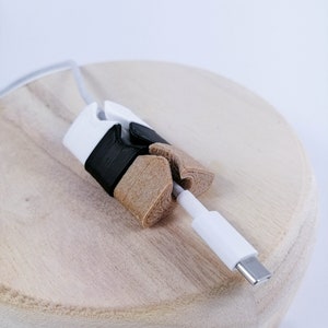 May include: A white and black cable organizer made of 3D printed plastic. The organizer is holding a white cable with a USB-C connector.